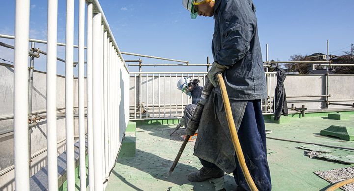 屋上の防水シートを電動ハンマーを使いコンクリートから剥がす斫り作業